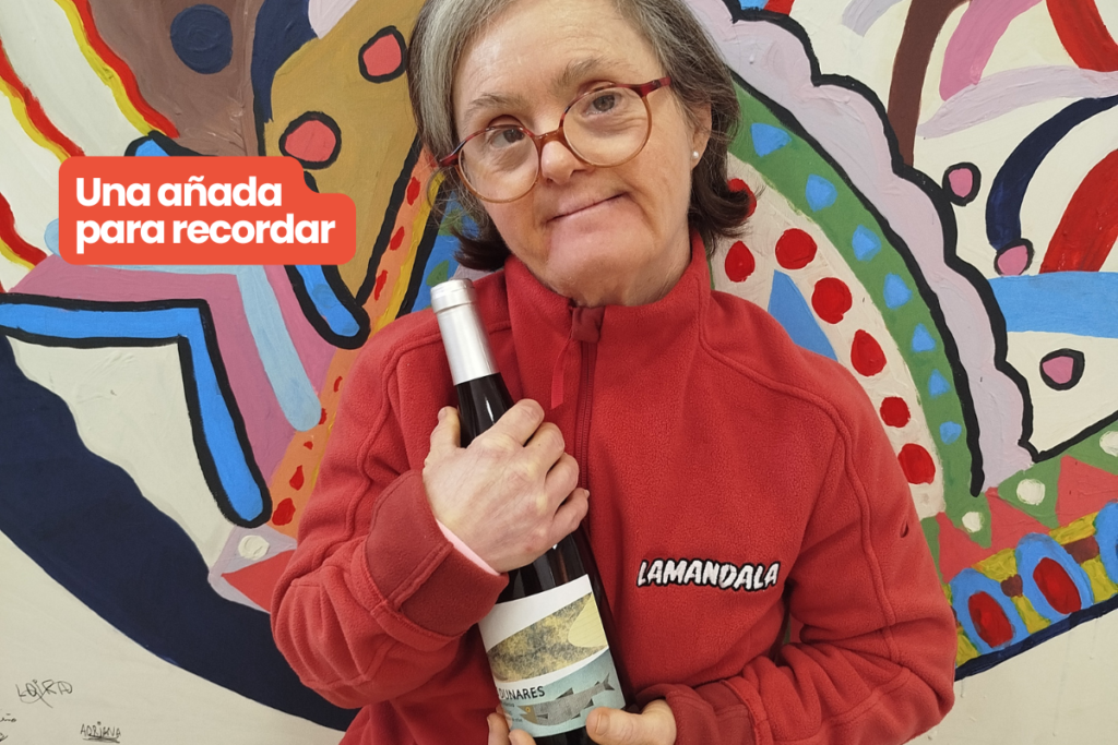 Maleni sostiene en sus brazos una botella de vino de los dunares frente al cuadro de Lamandala